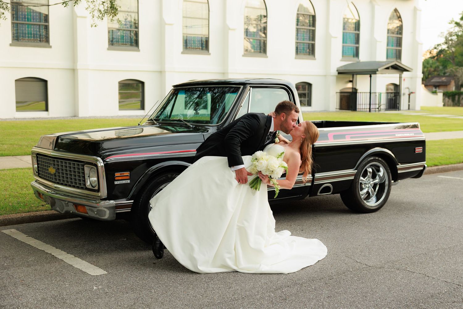 Bride and groom share romantic dip kiss beside vintage black Chevrolet pickup truck.