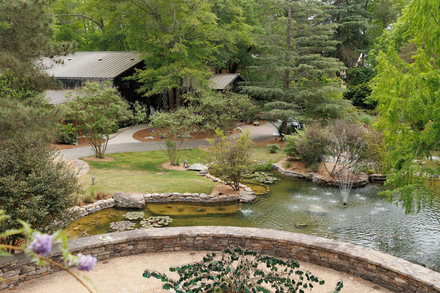 Aerial view of a serene Japanese garden with koi pond, stone walls, lush greenery, and a traditional pavilion.