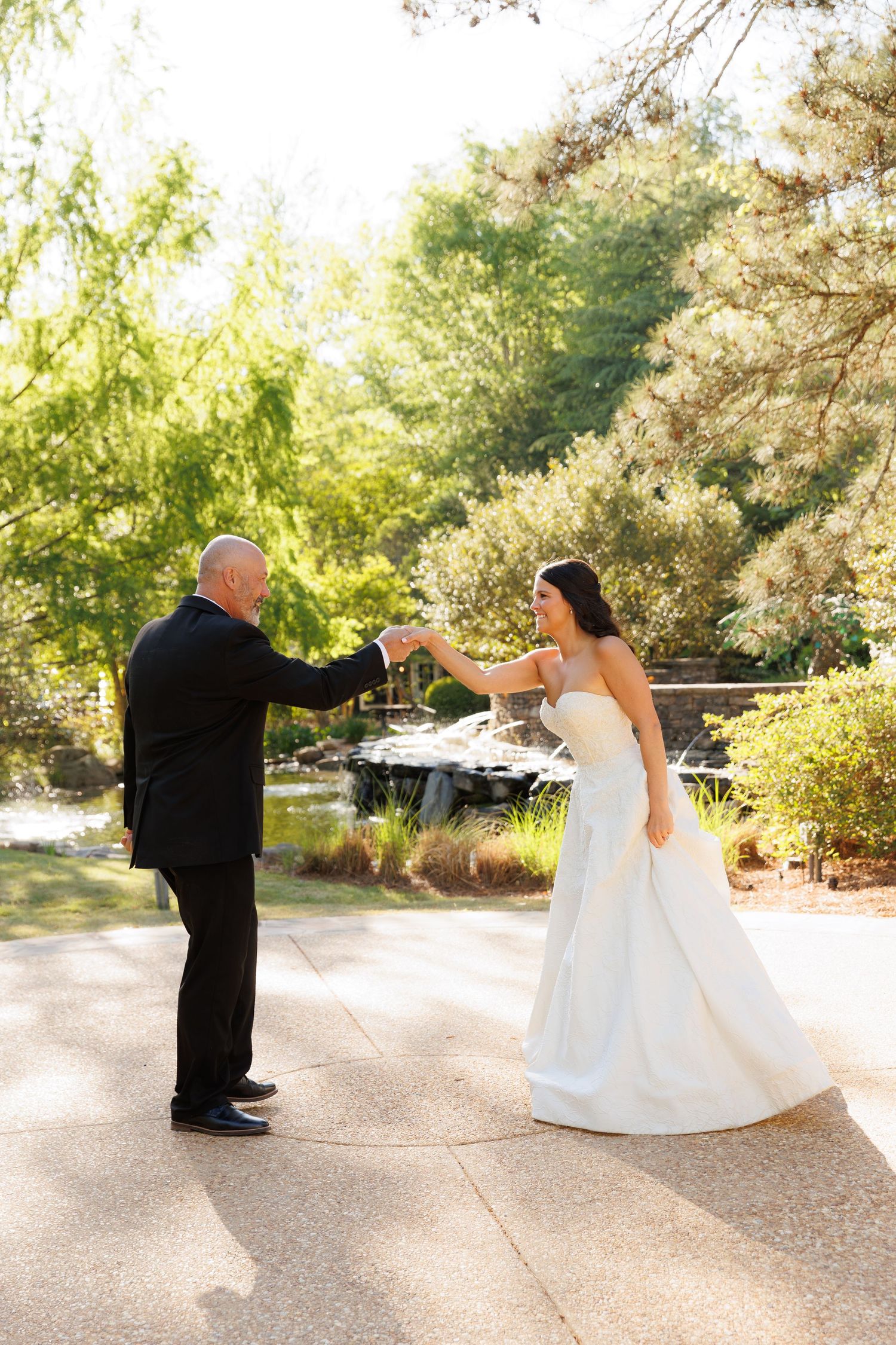 Bride and groom dancing outdoors in a lush garden, she in a white gown and he in a black suit.