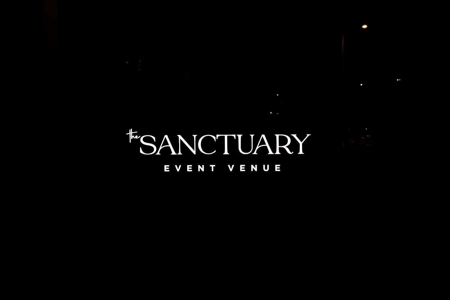 Illuminated Sanctuary Event Venue sign glowing white against a dark night sky background.