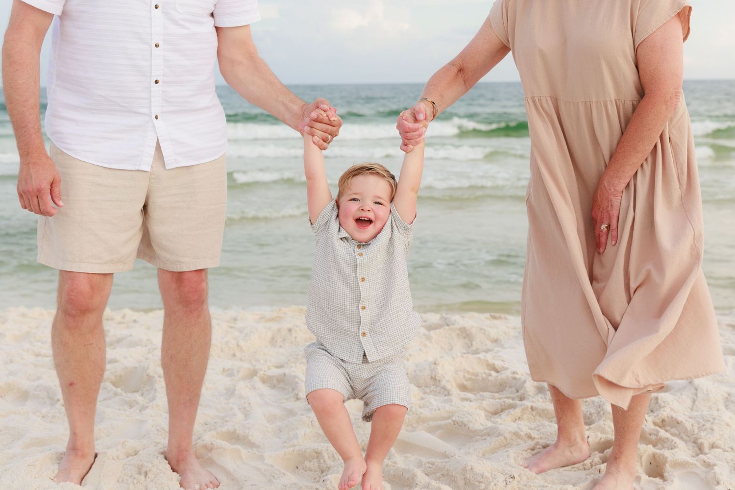 People holding hands and walking barefoot together on white sandy beach by turquoise ocean water.