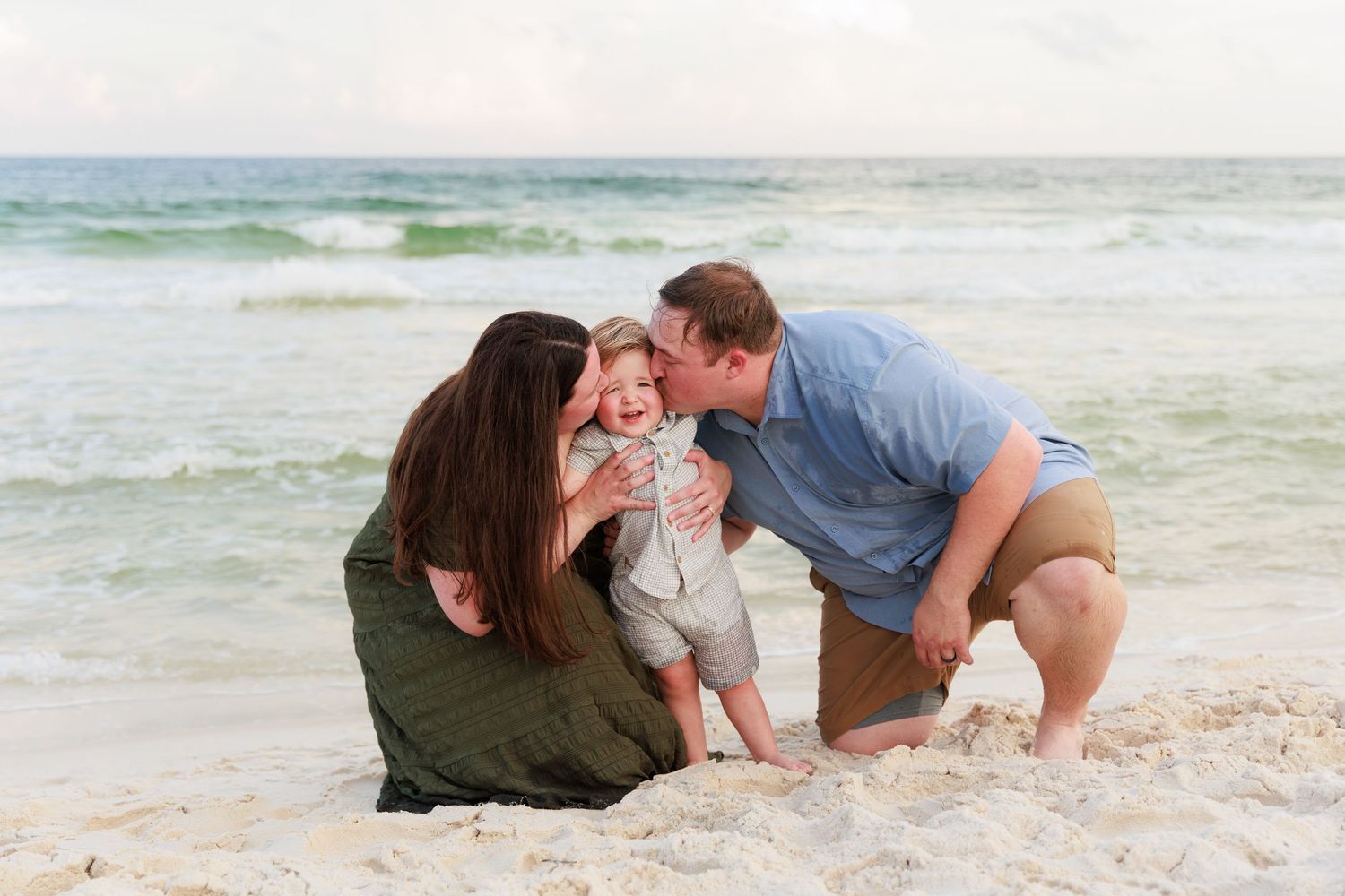 A family shares a tender moment together while playing in the sand at the beach during sunset.
