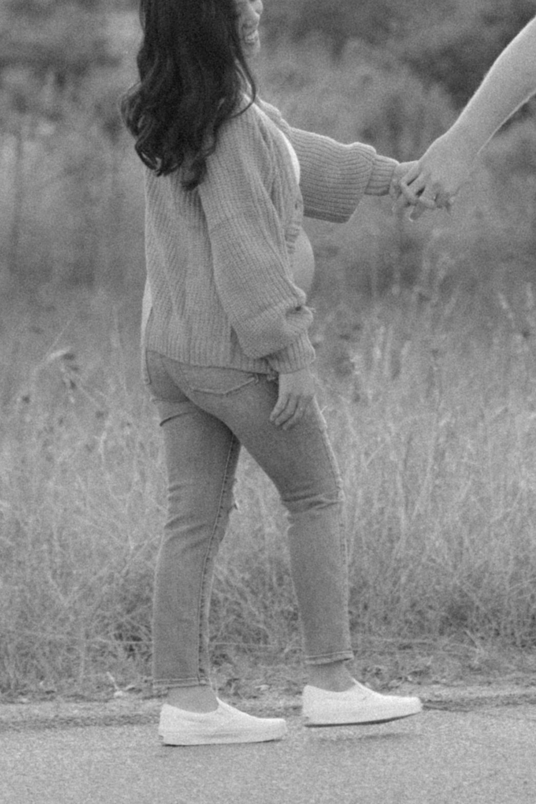 A series of black and white photos showing someone's legs wearing white sneakers walking through tall grass.