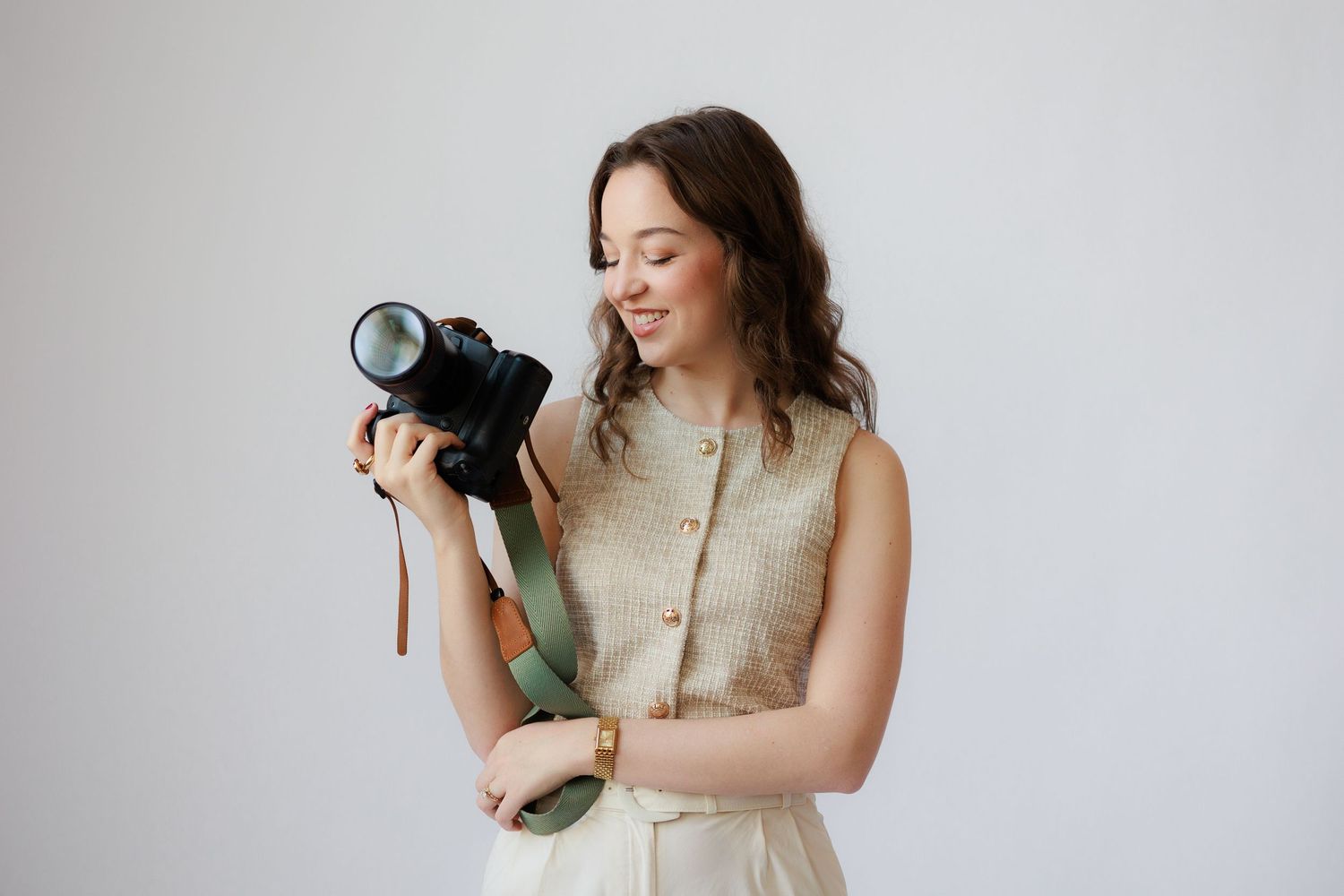 A photographer in a beige vest holds a professional camera while laughing against a white background.
