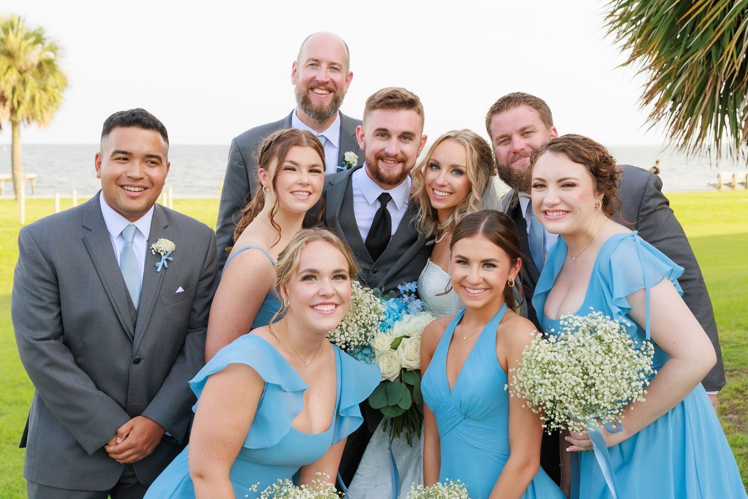 Wedding party poses for fun group photo with tropical palm trees in background.
