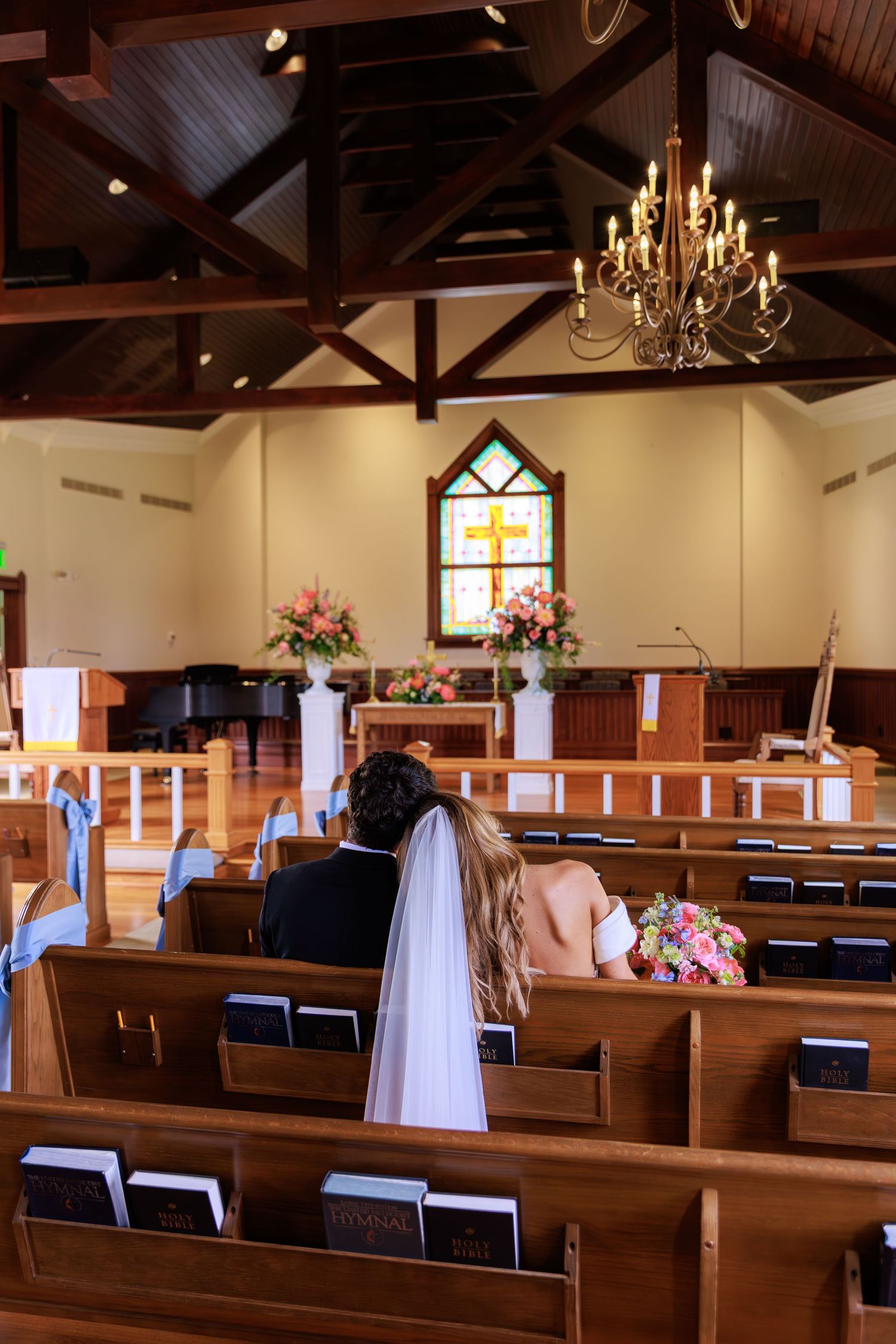 Interior of a traditional church sanctuary with wooden pews and chandeliers decorated for a wedding ceremony.