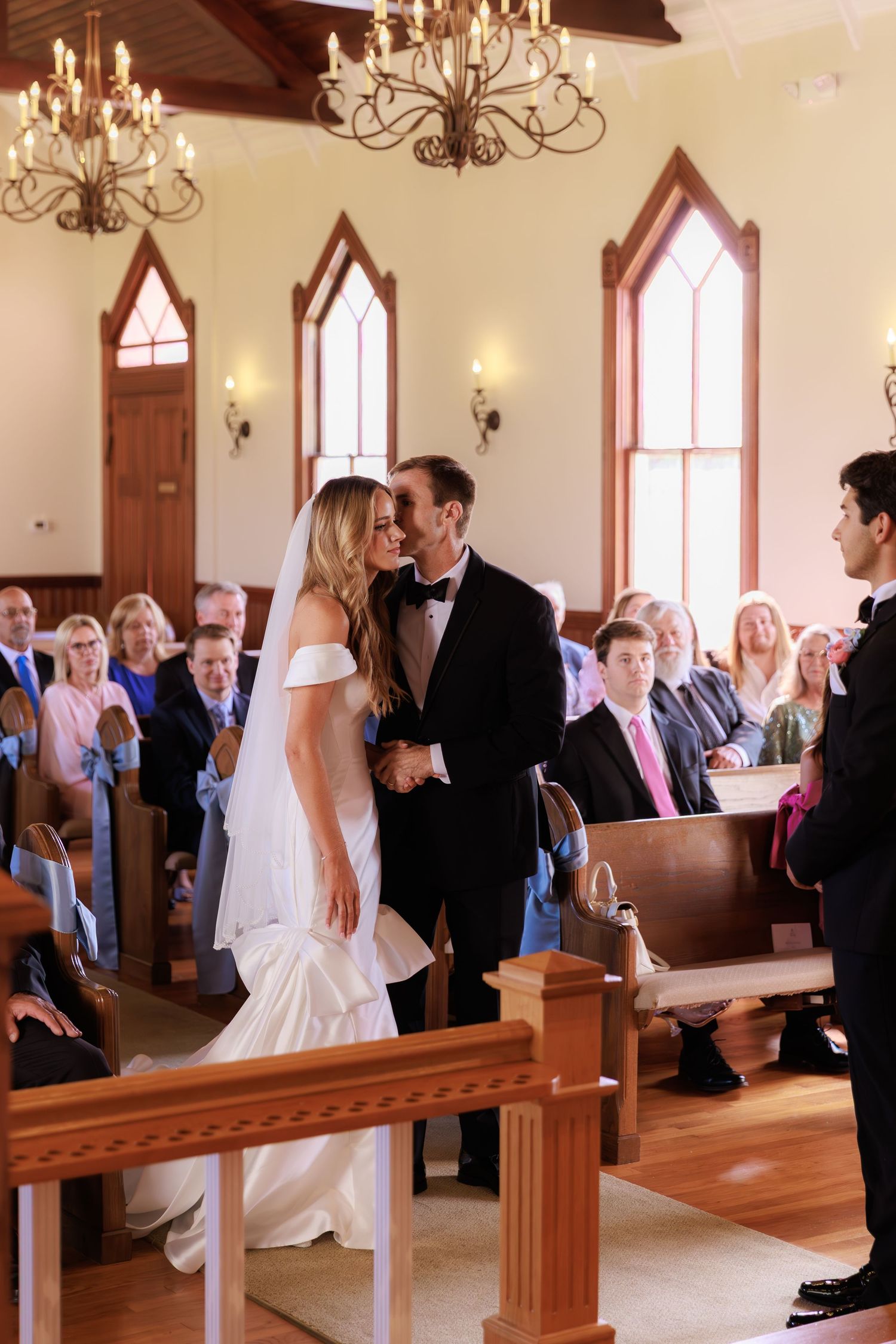 Wedding ceremony taking place in a traditional church with stained glass windows and wooden pews.