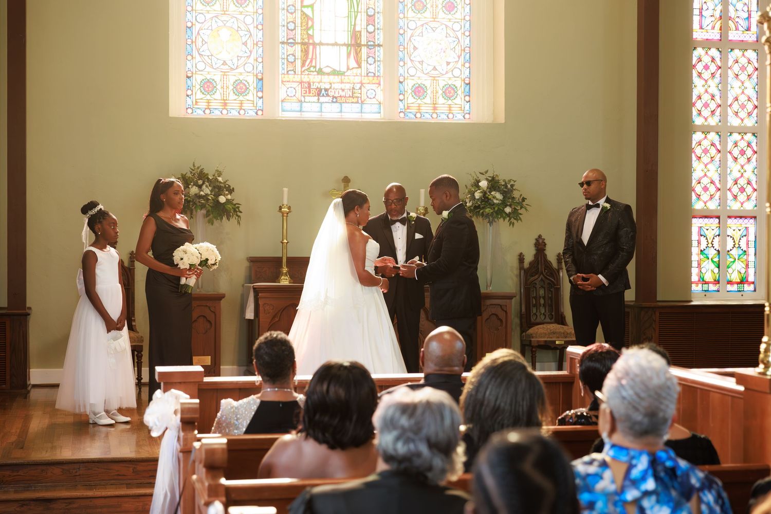 Wedding ceremony taking place in a traditional church sanctuary with stained glass windows and wooden pews.