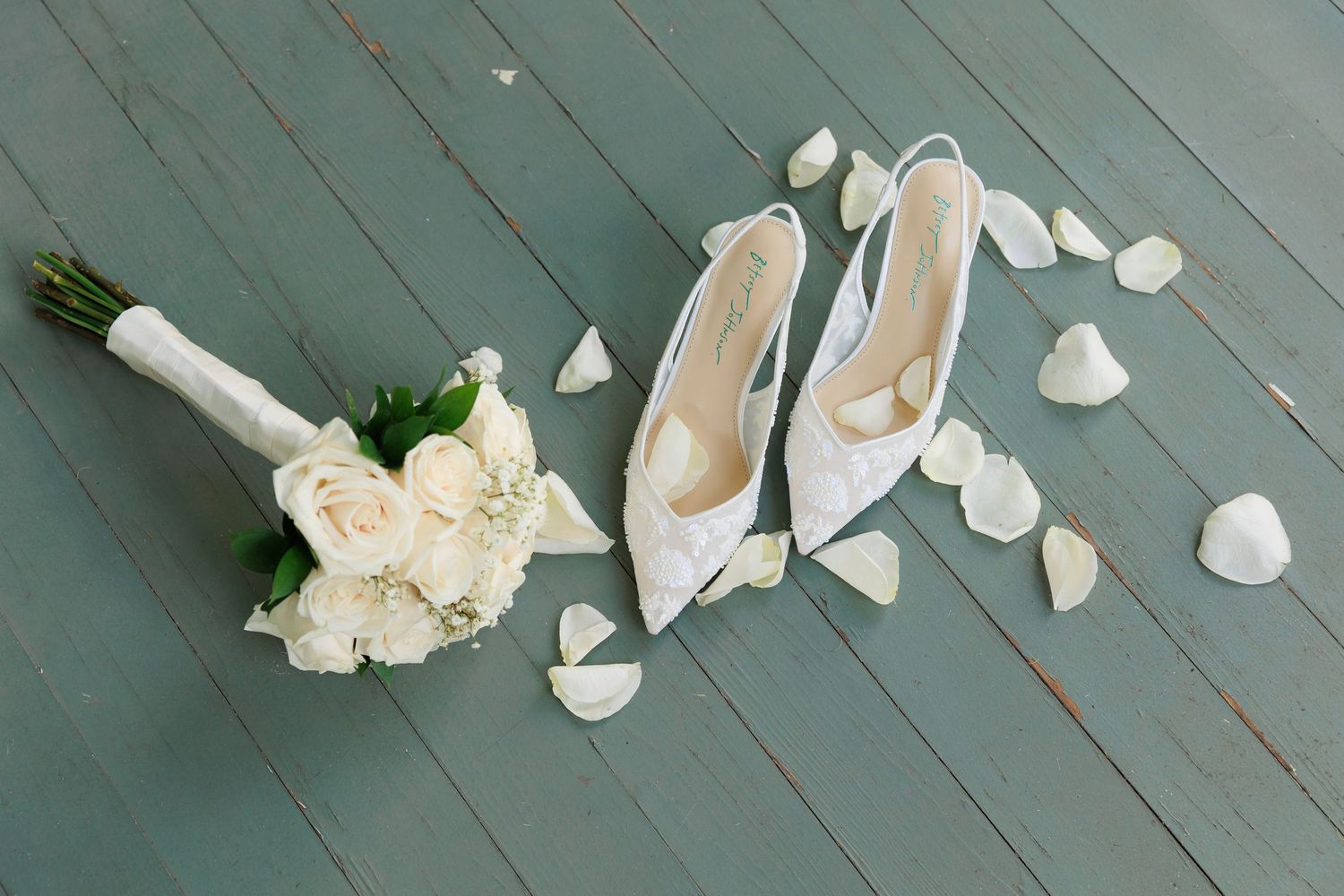 White rose petals and flowers scattered on a rustic blue wooden surface create a romantic composition.
