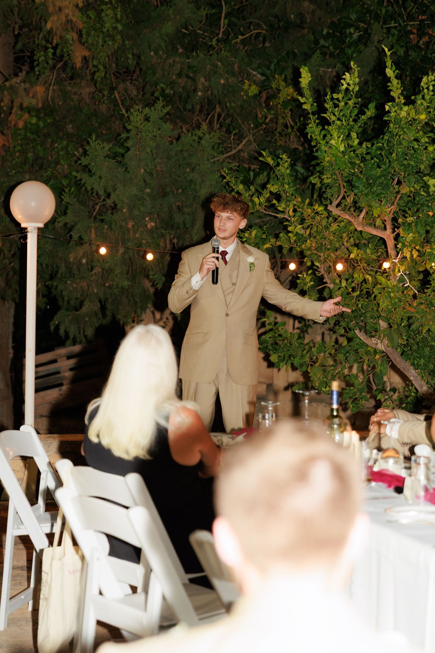 Wedding guests dance and celebrate at an outdoor evening reception with white tablecloths and string lights.
