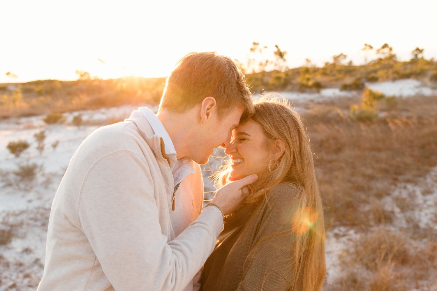Romantic couple embraces during golden hour sunset on a sandy beach with glowing sunlight behind them.