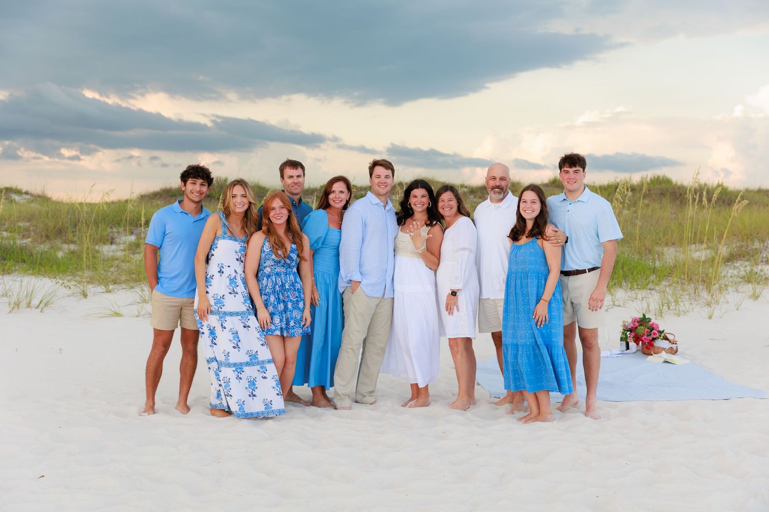 Family group wearing coordinated blue and white outfits posing together on a sandy beach at sunset.