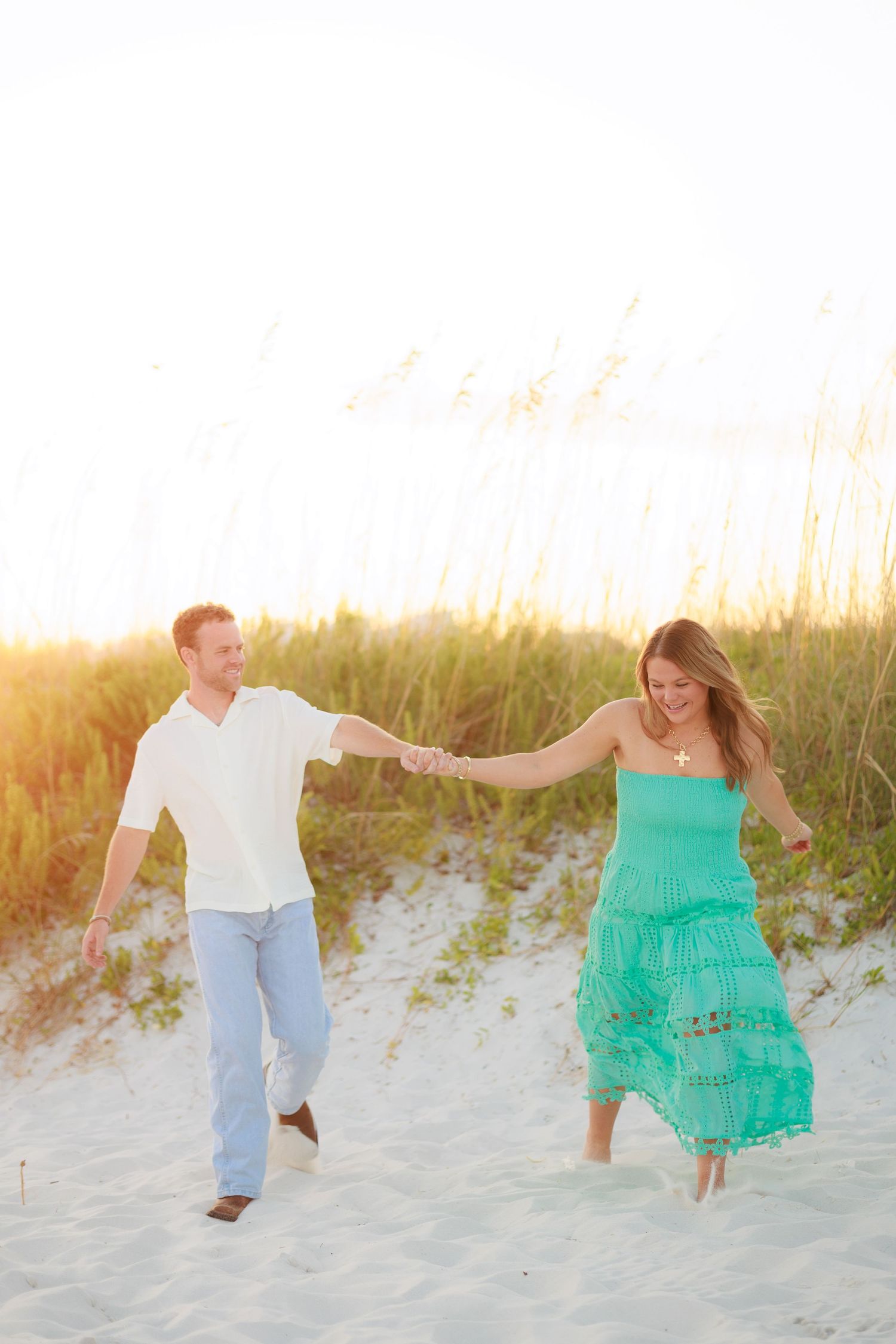 Playful couple runs and jumps along sandy beach dunes during golden hour.