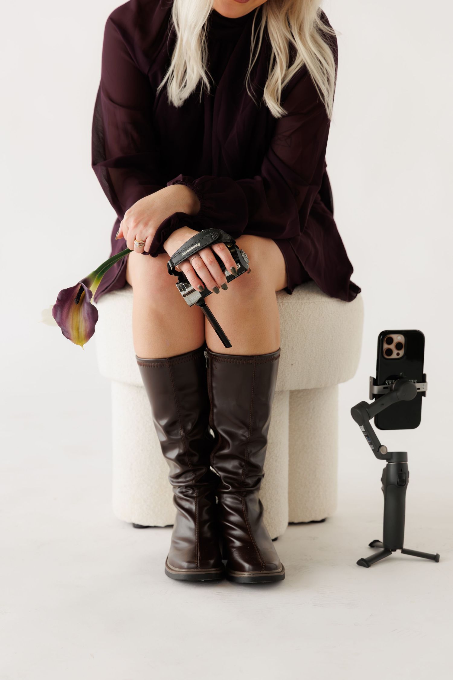 Close-up view of black leather boots and dark clothing against white studio backdrop.