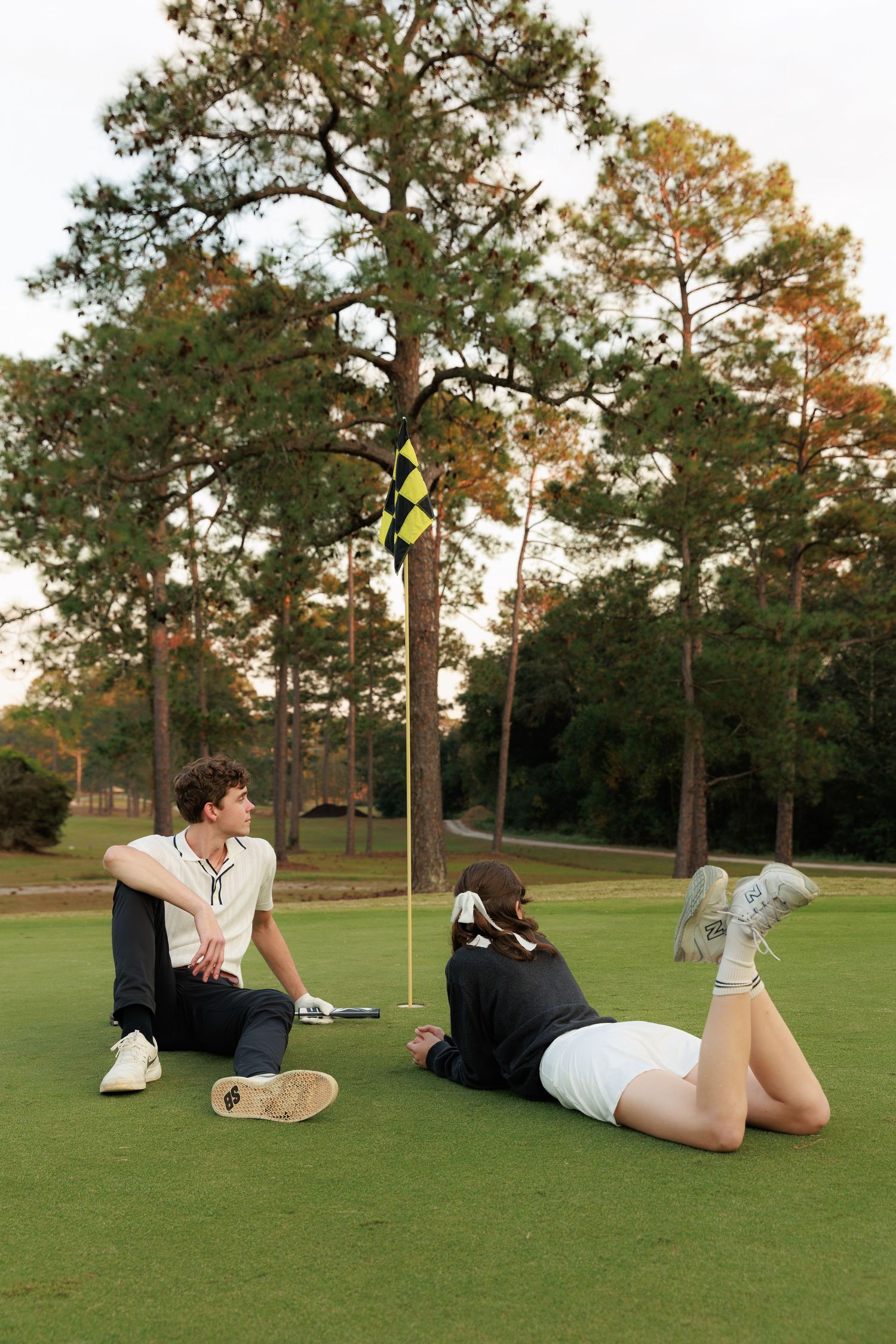 A person lies on a golf course green in a relaxed pose during golden hour lighting.