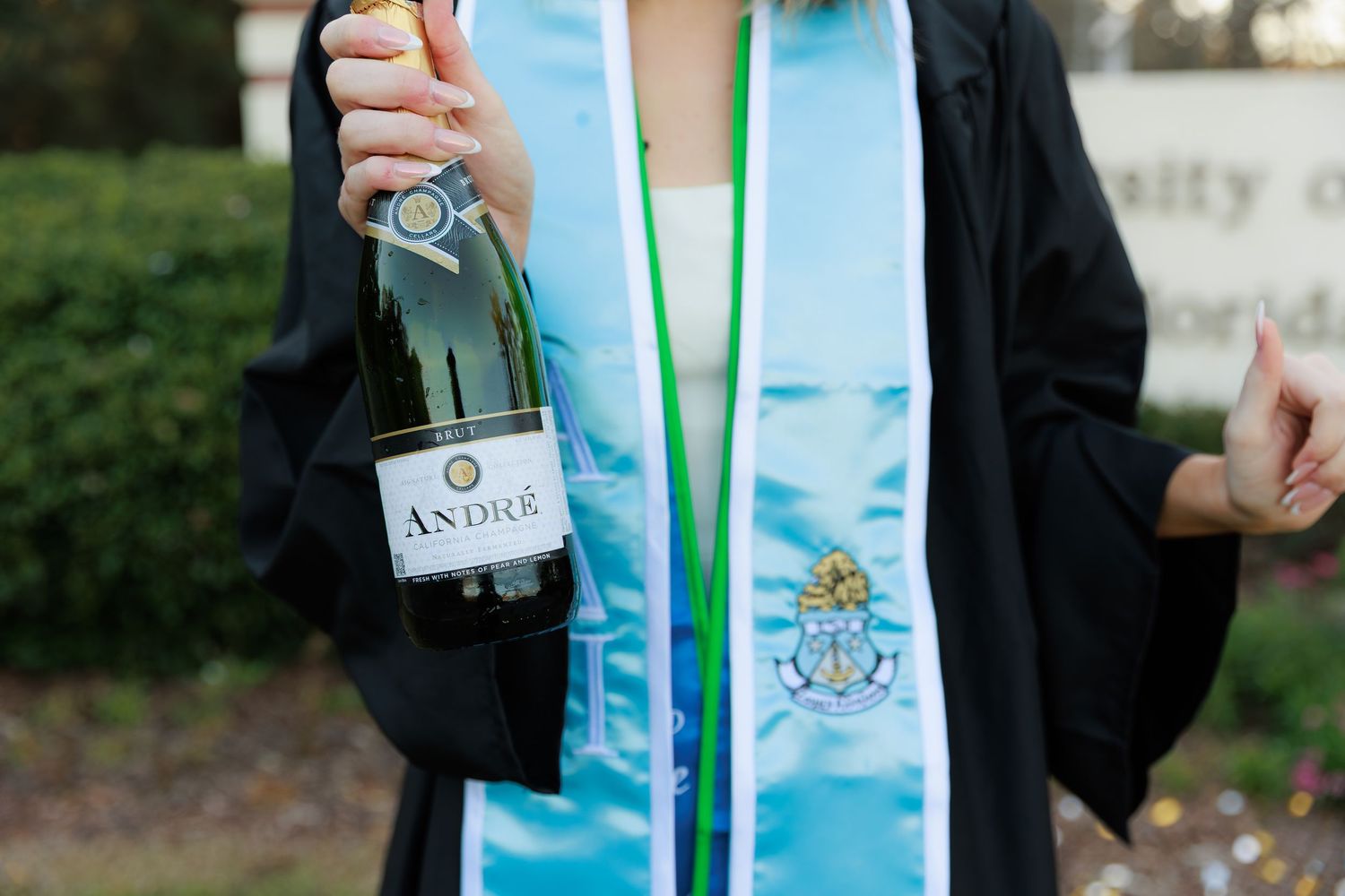 A person wearing a light blue graduation stole holds a champagne bottle during a celebration.