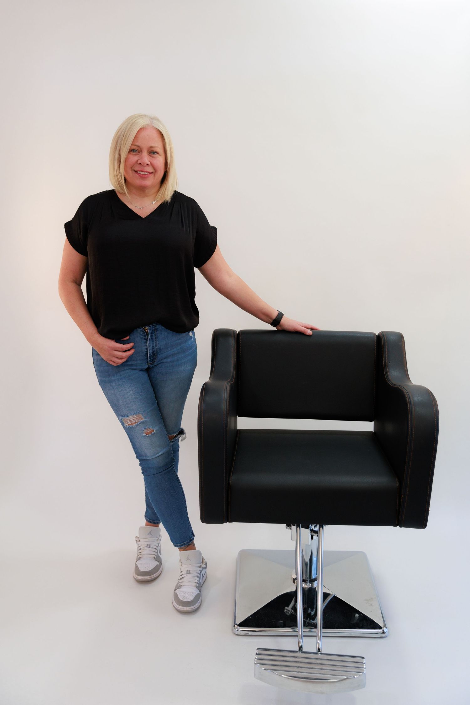 Casual pose next to black salon chair wearing comfortable everyday attire.