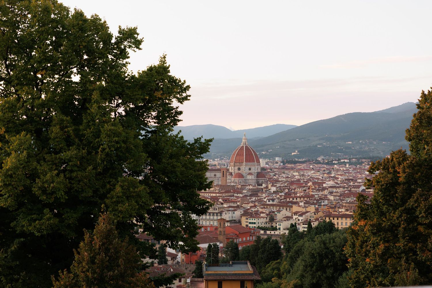 Panoramic view of Florence Italy skyline with the iconic Duomo cathedral dome rising above terracotta rooftops at dusk.