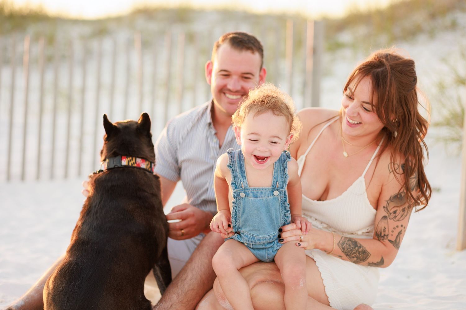 Happy family with a toddler and black dog enjoying a sunny beach day together.