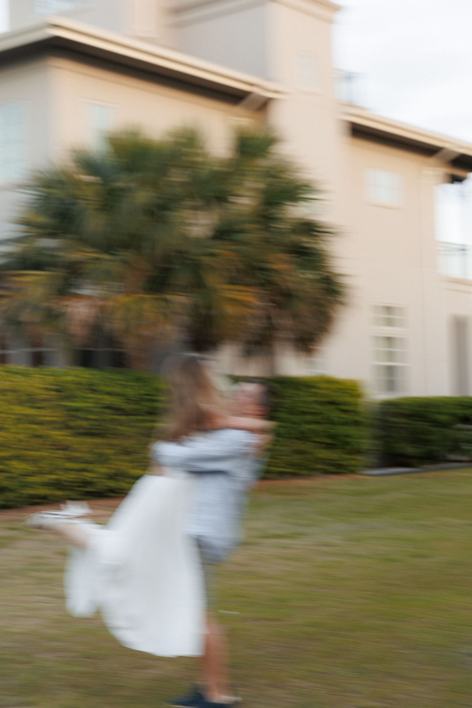 Blurred motion shot of a couple spinning together outdoors near a building with palm trees.