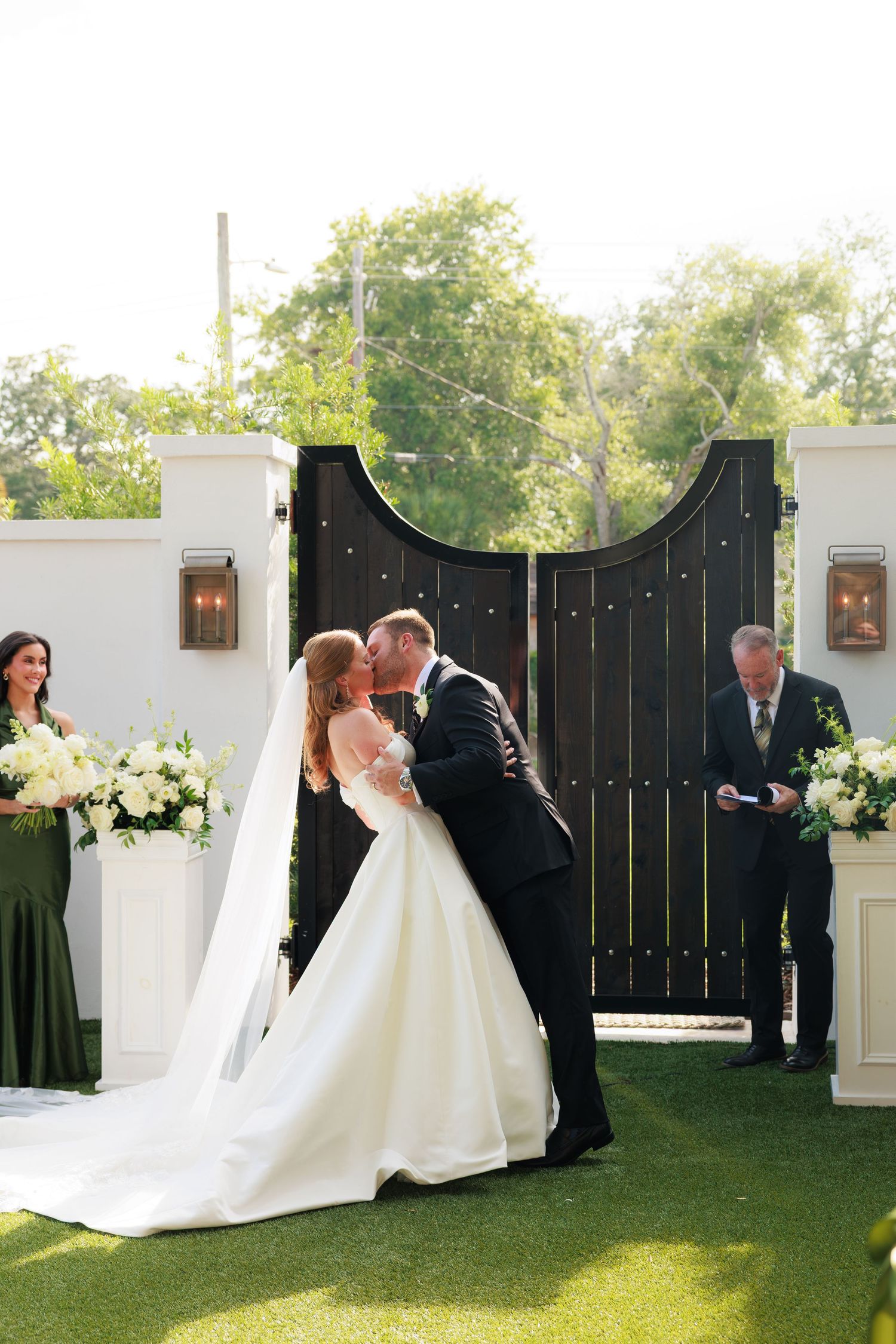 Bride and groom share first kiss at elegant outdoor wedding ceremony.