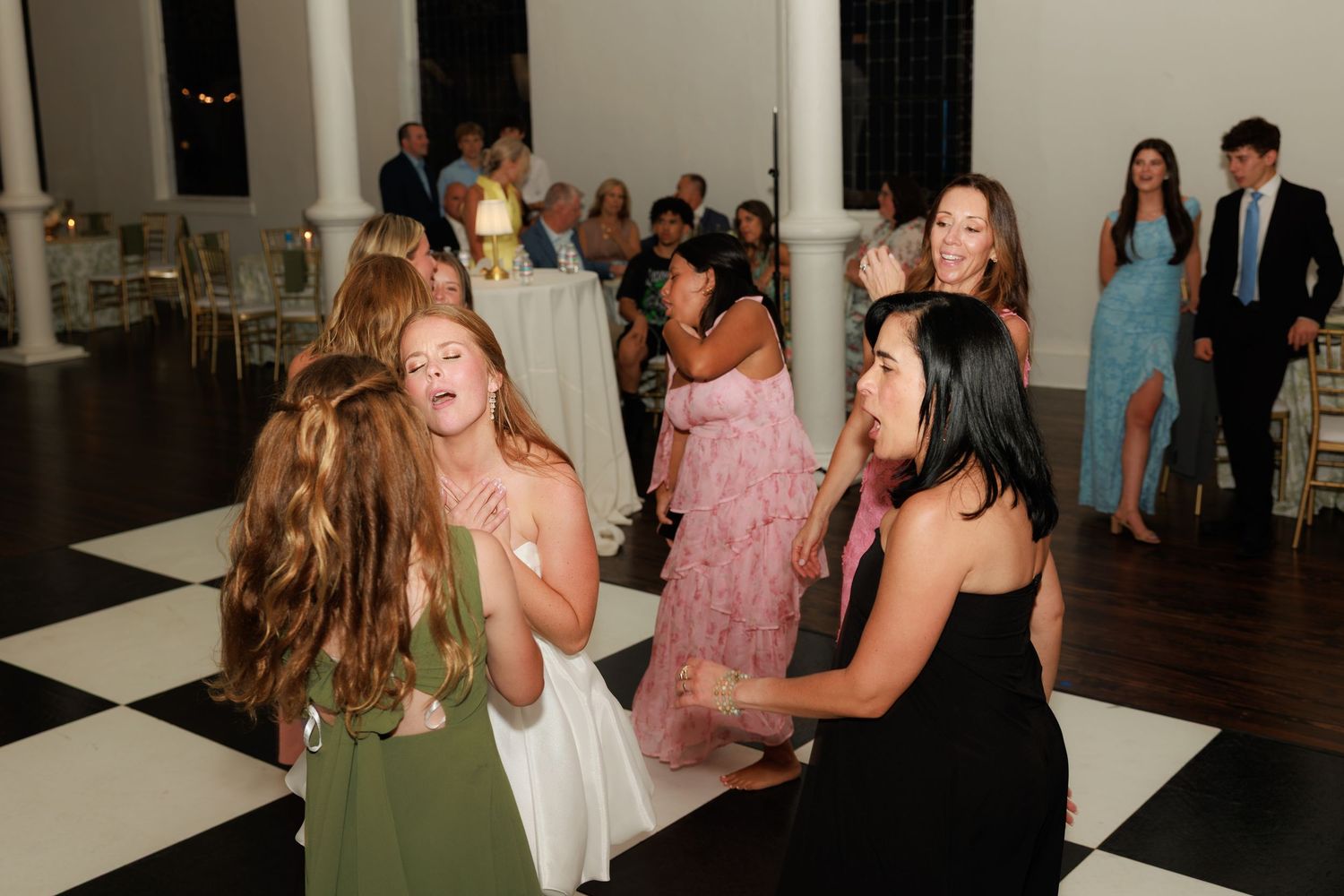 Guests dancing joyfully on black and white checkered dance floor at elegant wedding reception.