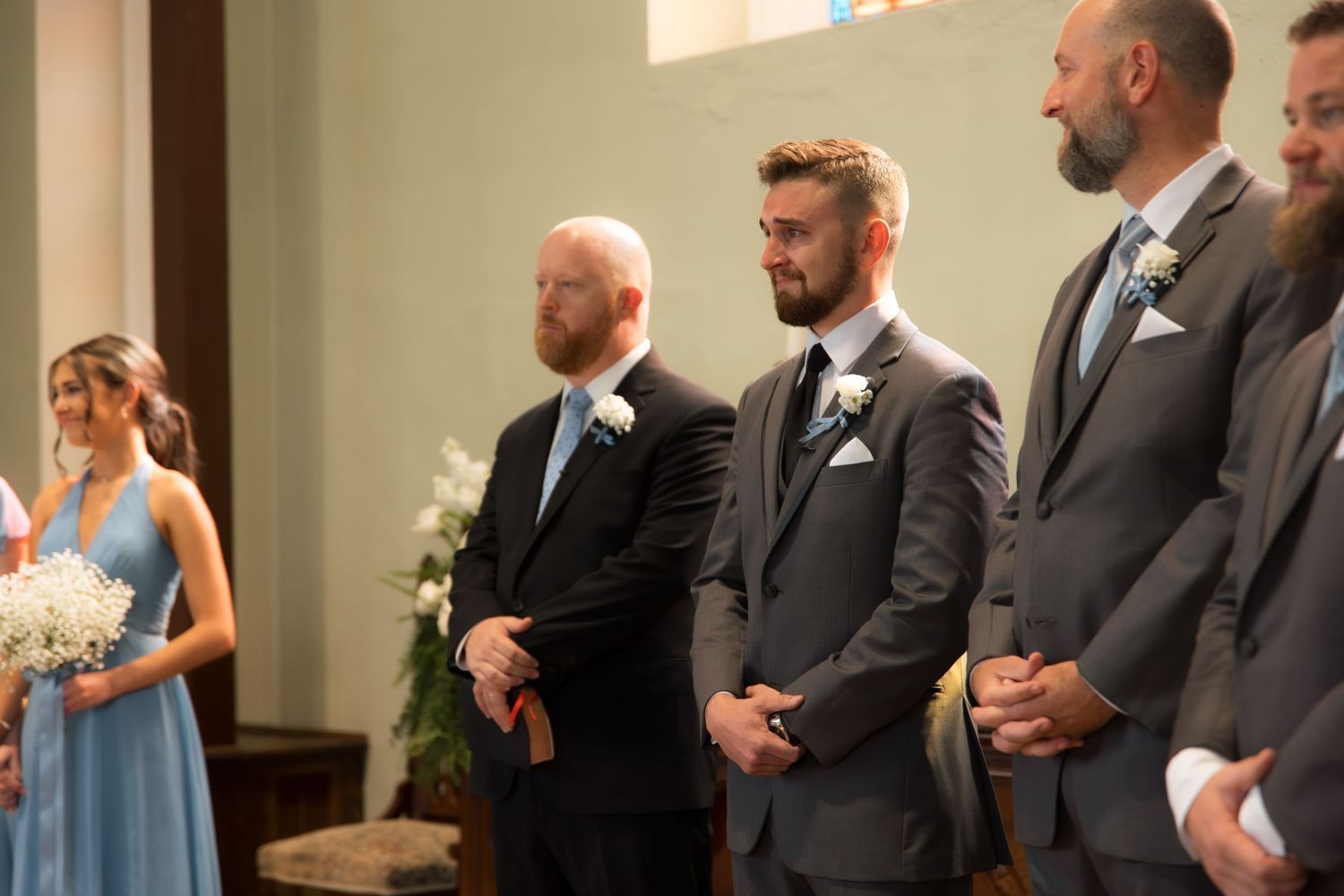 Wedding party members line the aisle during indoor church ceremony.