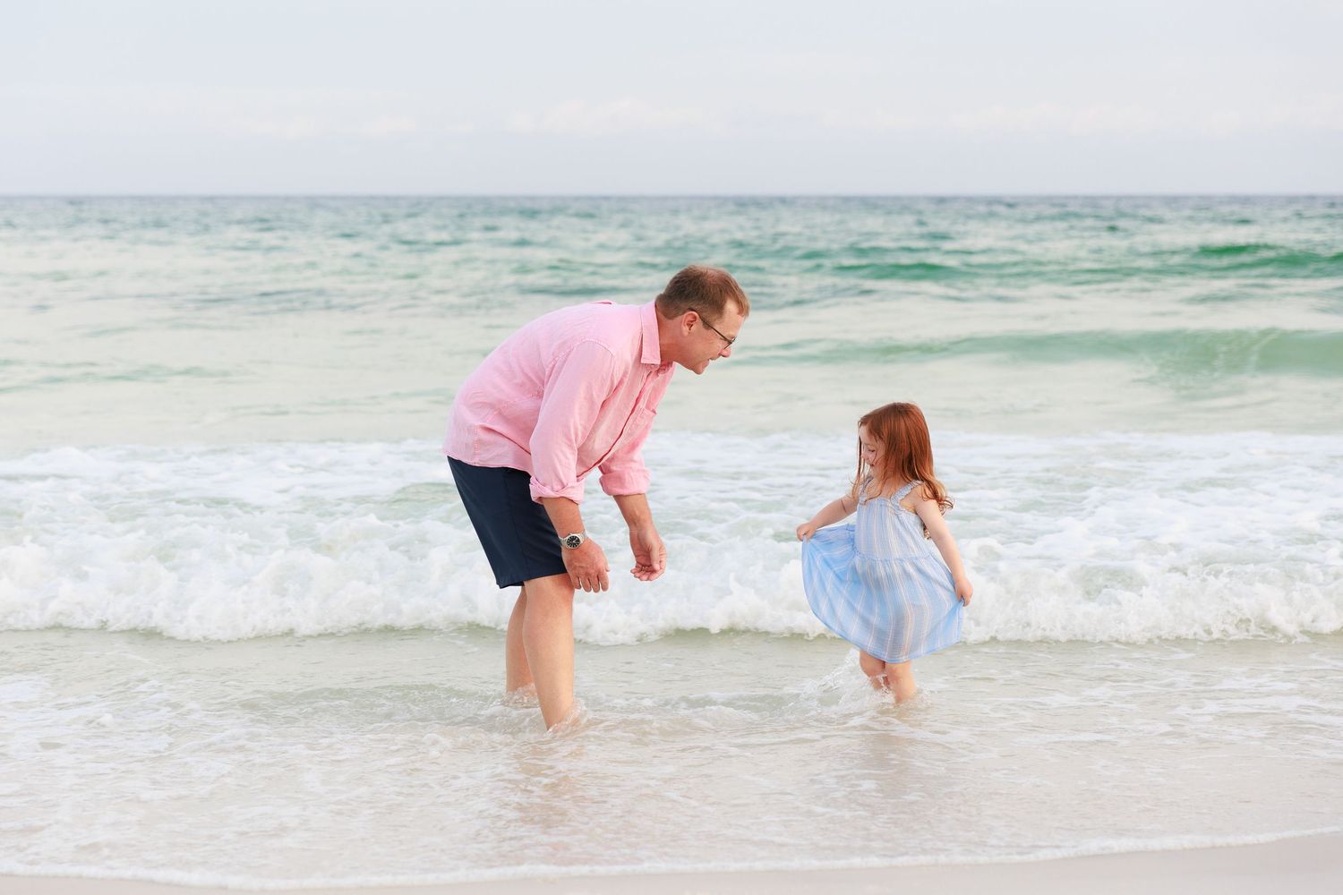 Two people playing together in the shallow ocean waves at the beach on a sunny day.