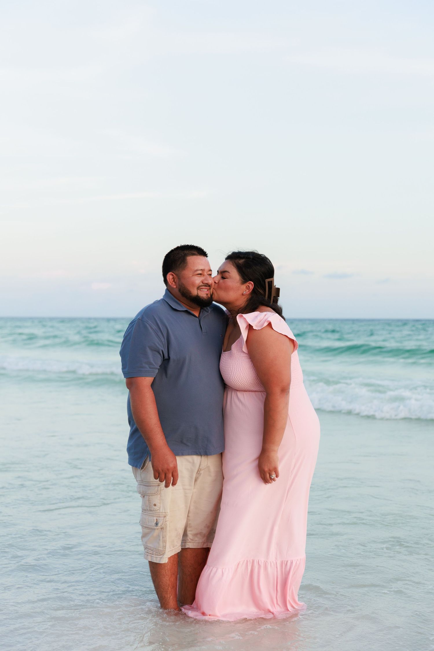 A couple shares an intimate moment while standing in the ocean waves at sunset.