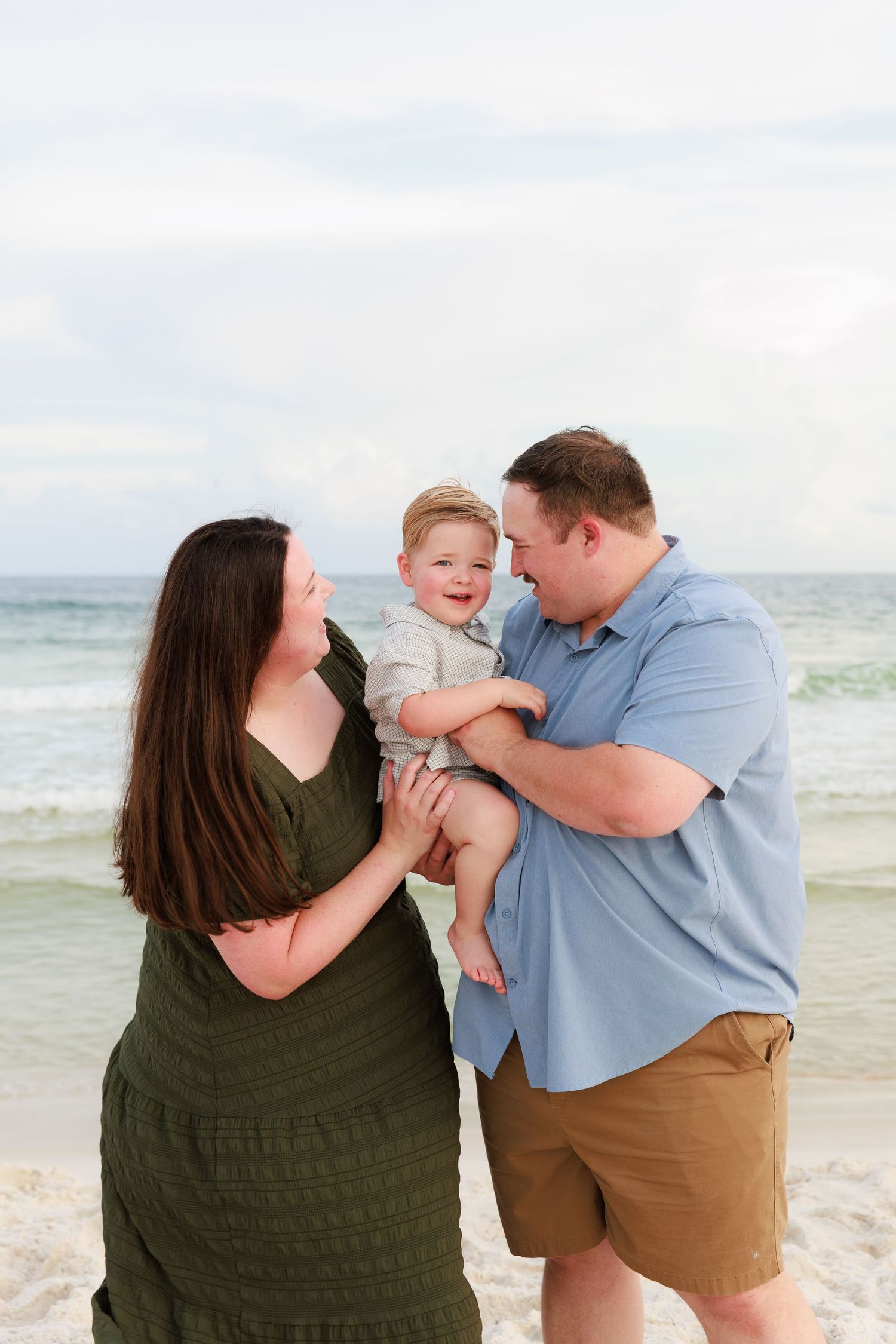 A family plays together and shares joyful moments on a sunny beach with ocean waves in the background.
