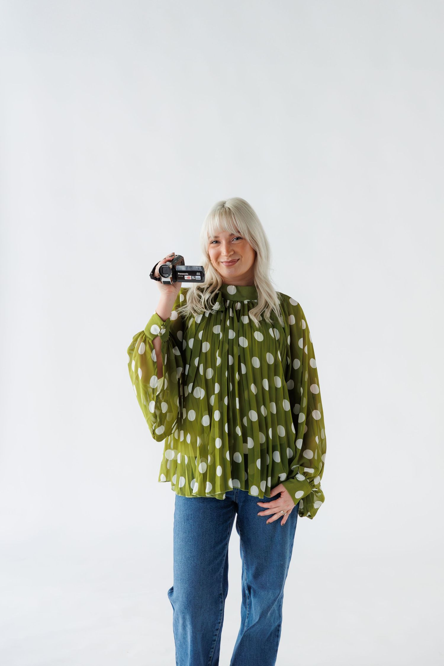 Person wearing a green polka dot blouse and blue jeans poses in three different casual stances against white background.