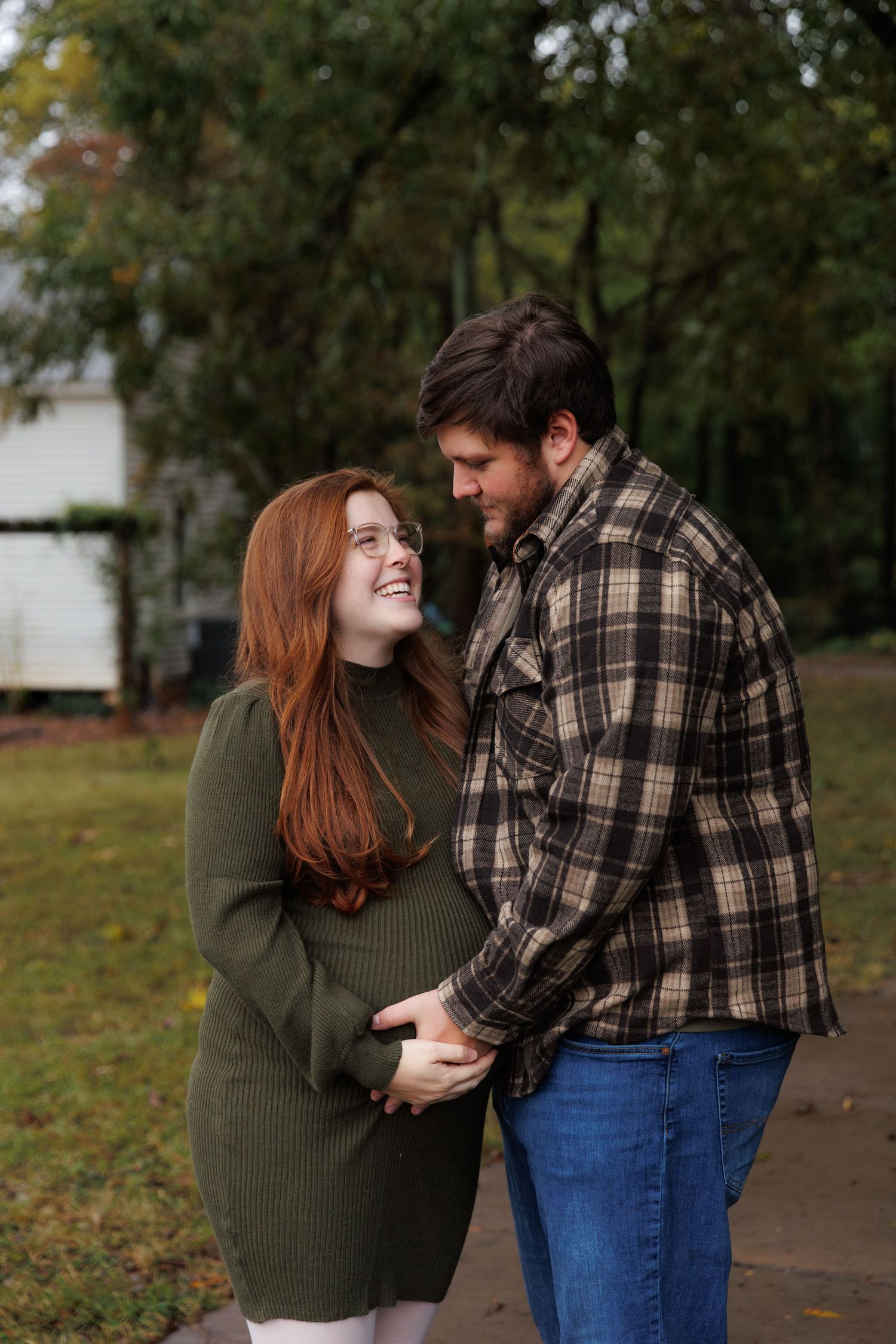 A couple shares intimate moments while standing together on fallen autumn leaves with trees in background.