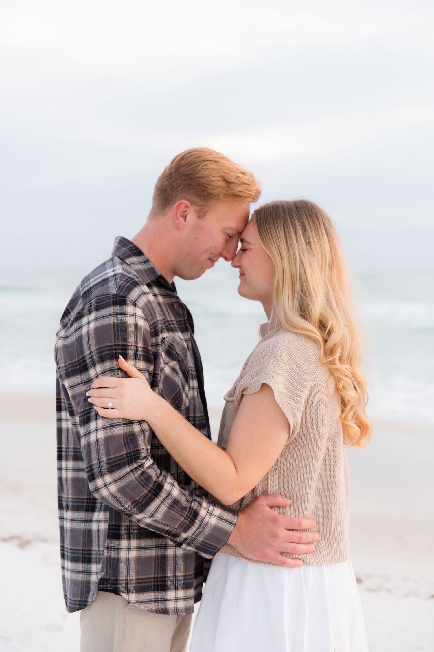 Intimate moment between couple in casual wear sharing tender embrace on cloudy beach.