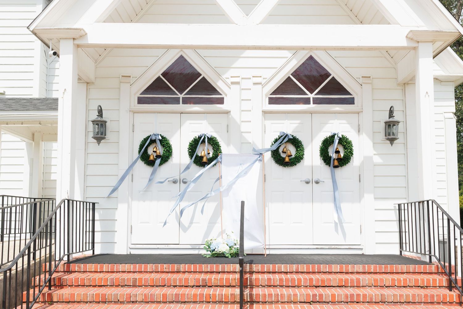White church entrance with green Christmas wreaths and red brick steps decorated for the holiday season.