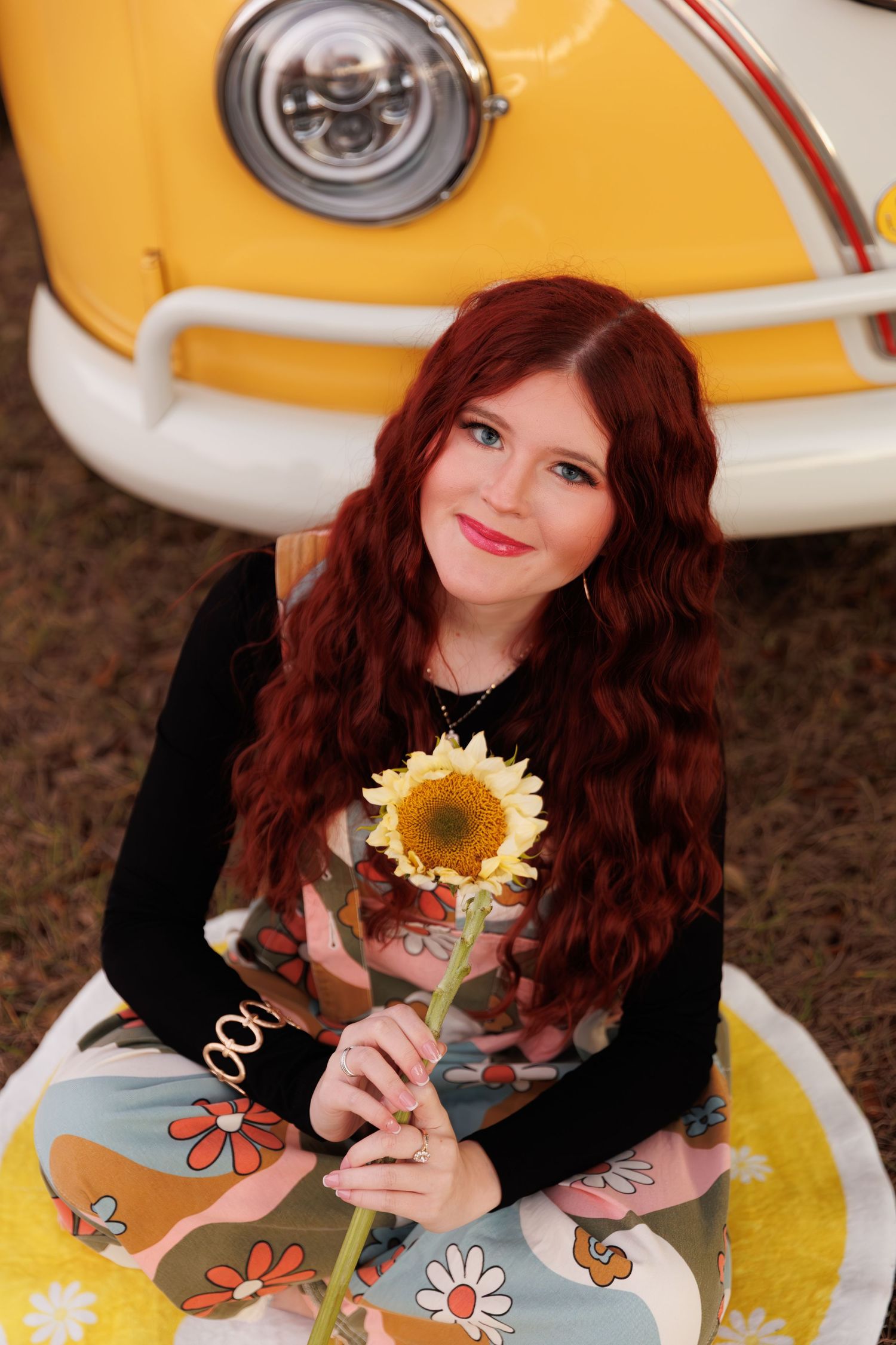 A whimsical fashion shoot featuring a sunflower prop against a classic Volkswagen van backdrop.