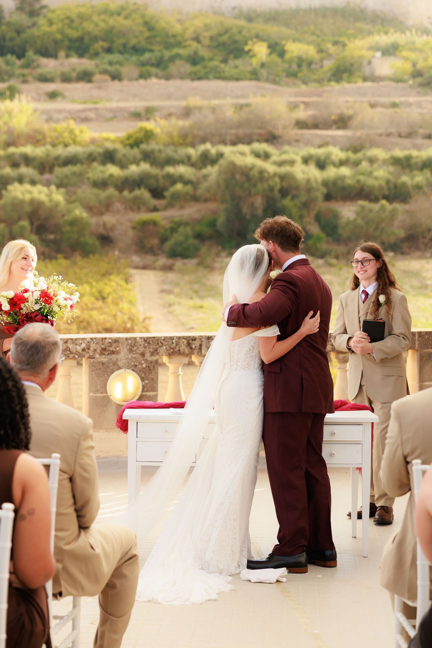 Wedding ceremony guests stand in a row at an outdoor venue with scenic mountain views in the background.
