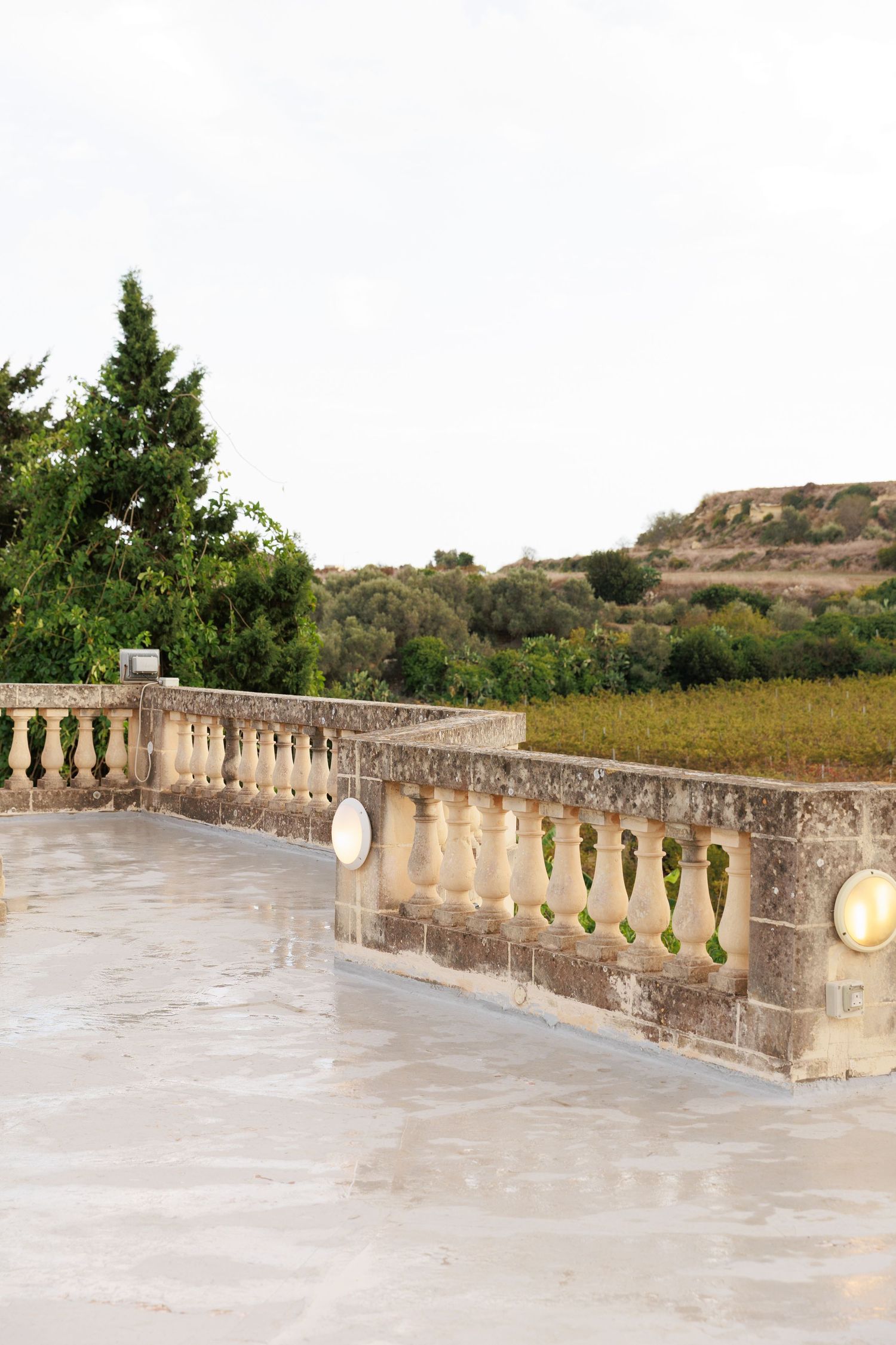 Stone balustrade with decorative balusters extends along a terrace with green vegetation visible in the background.
