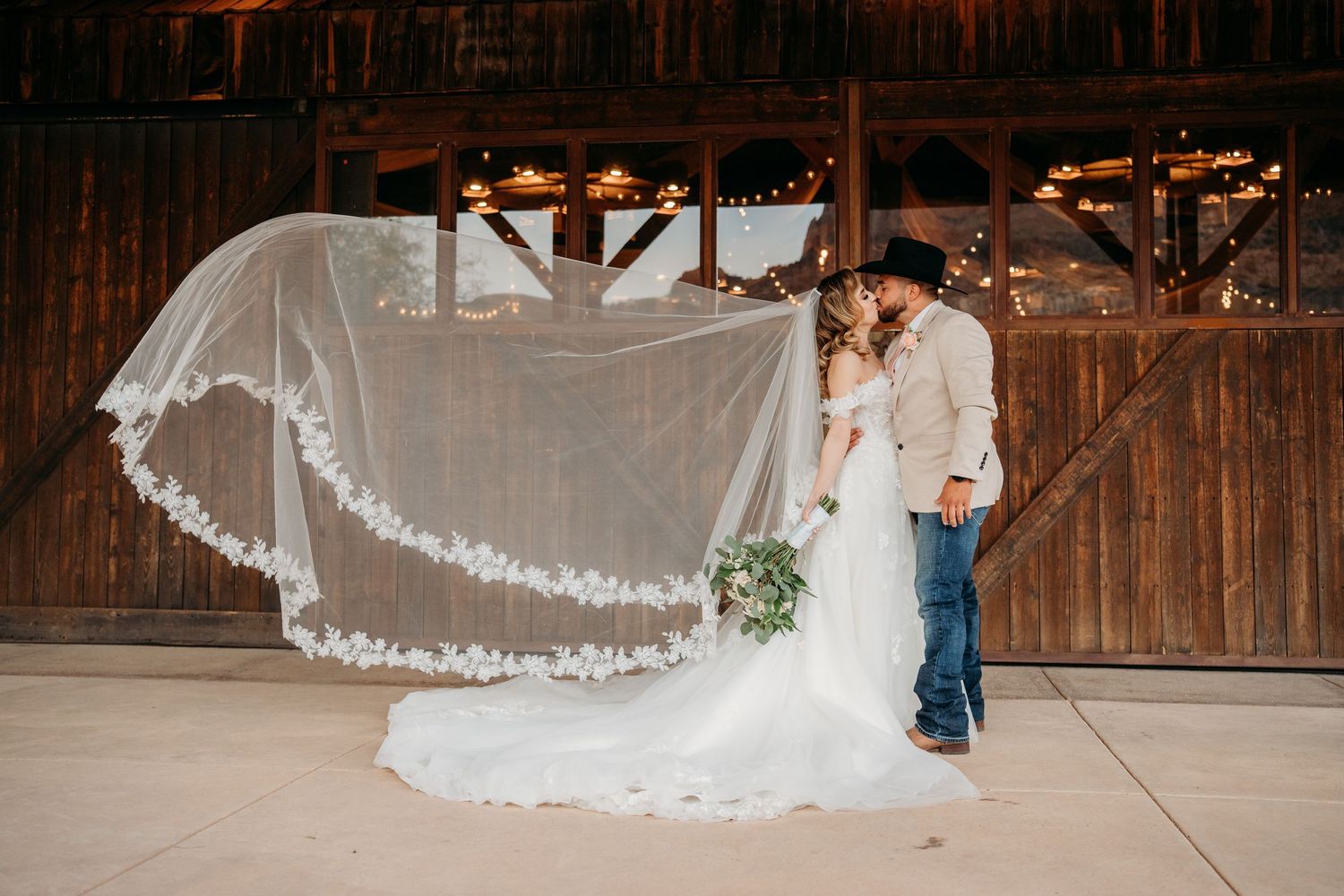 A romantic wedding moment captured in a rustic barn setting with a flowing lace veil caught in the breeze.