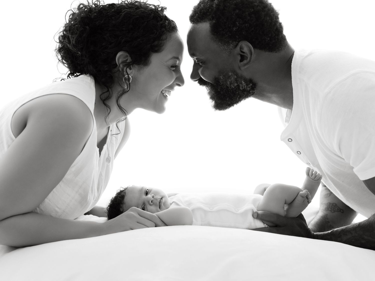 Black and white photo of smiling parents leaning over newborn baby in a tender family portrait.