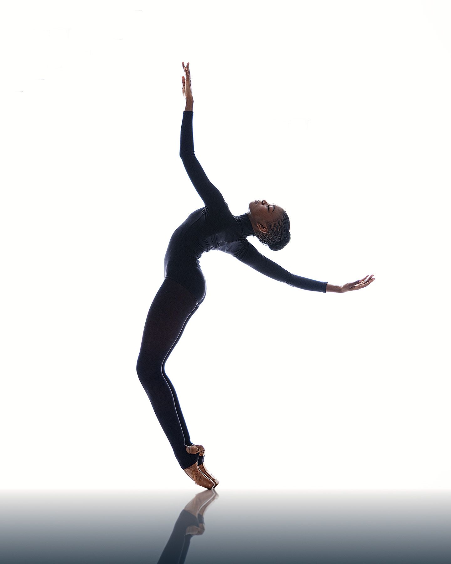 A dancer in black attire performs a graceful backward arch movement against a light gray background.