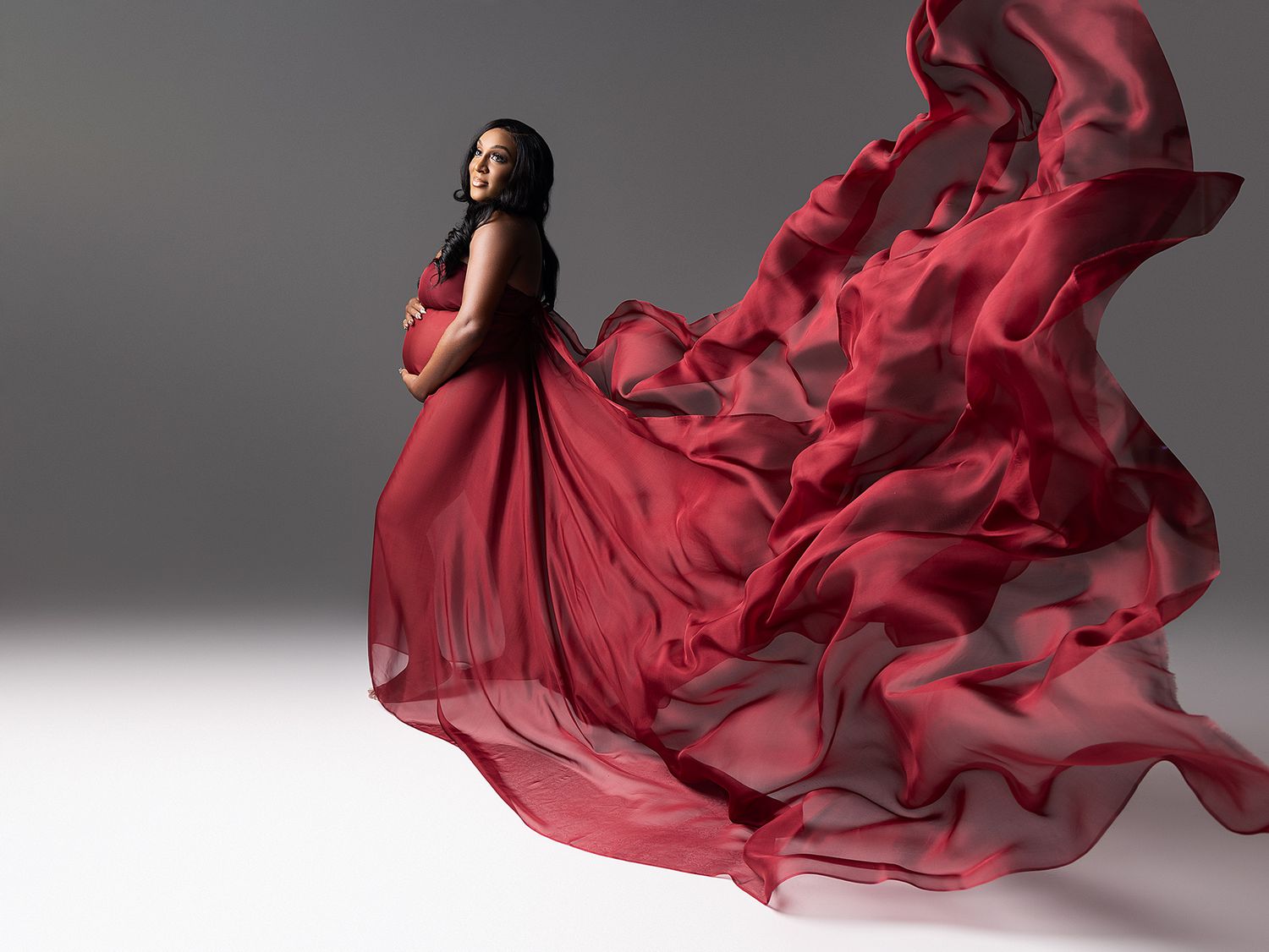 Flowing red silk fabric billows gracefully against a gray studio backdrop creating dramatic movement and texture.