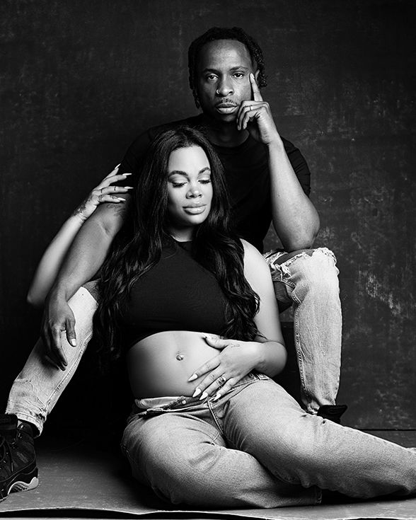 Black and white maternity photo of a pregnant woman and man posing together in a professional studio portrait.