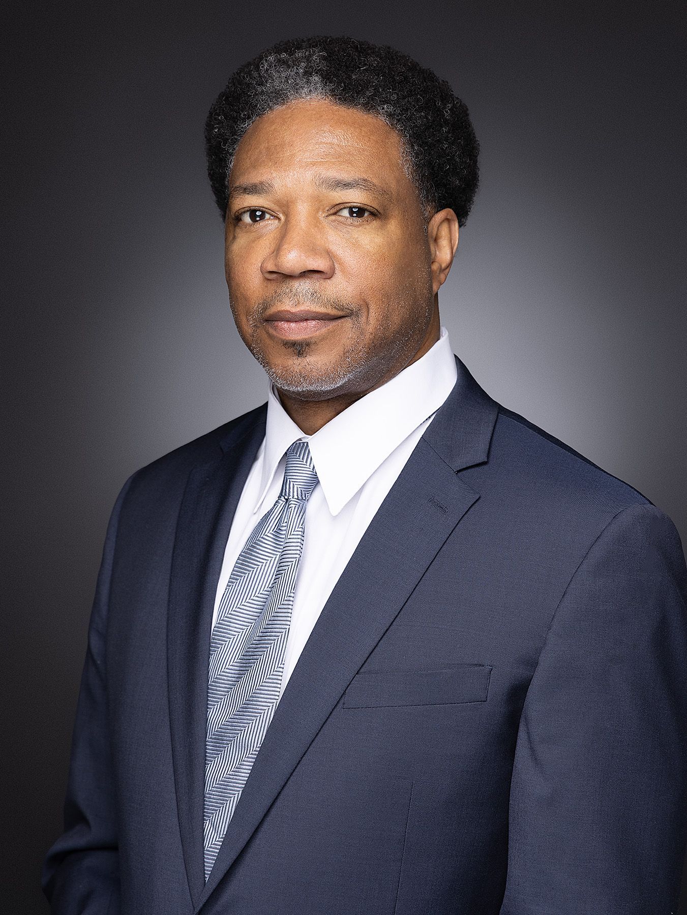 Professional headshot of person in navy suit and striped tie against gray background shown from different angles.