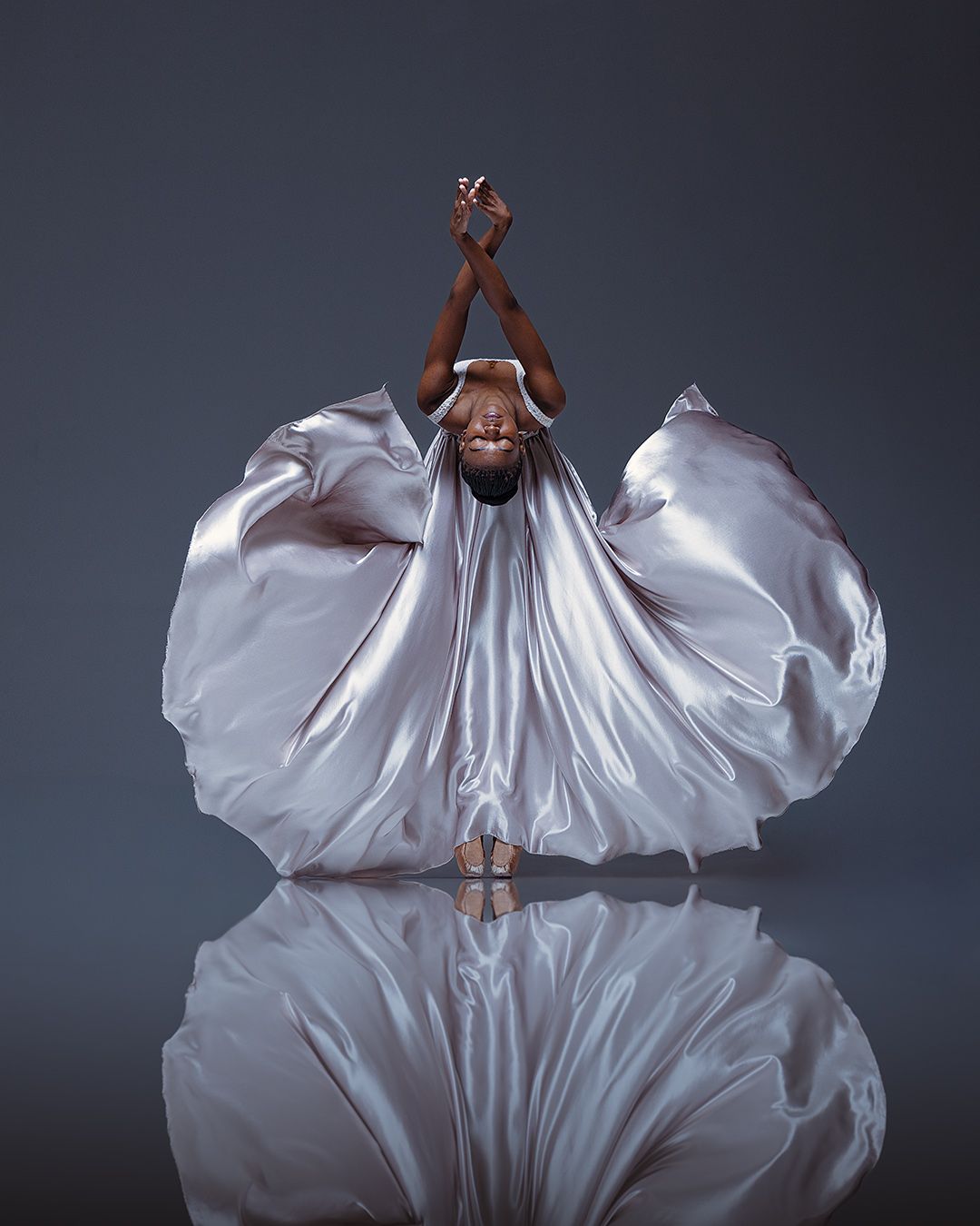 A dancer in a flowing white dress creates a dramatic silhouette against a dark background as fabric billows around them.