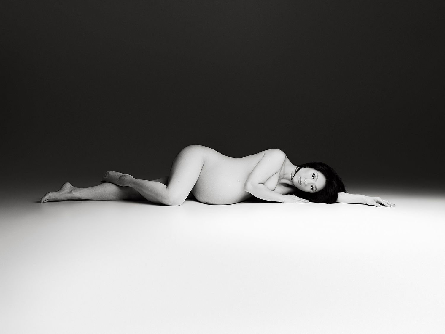 Black and white artistic photograph of a figure reclining on a white surface in minimalist composition.