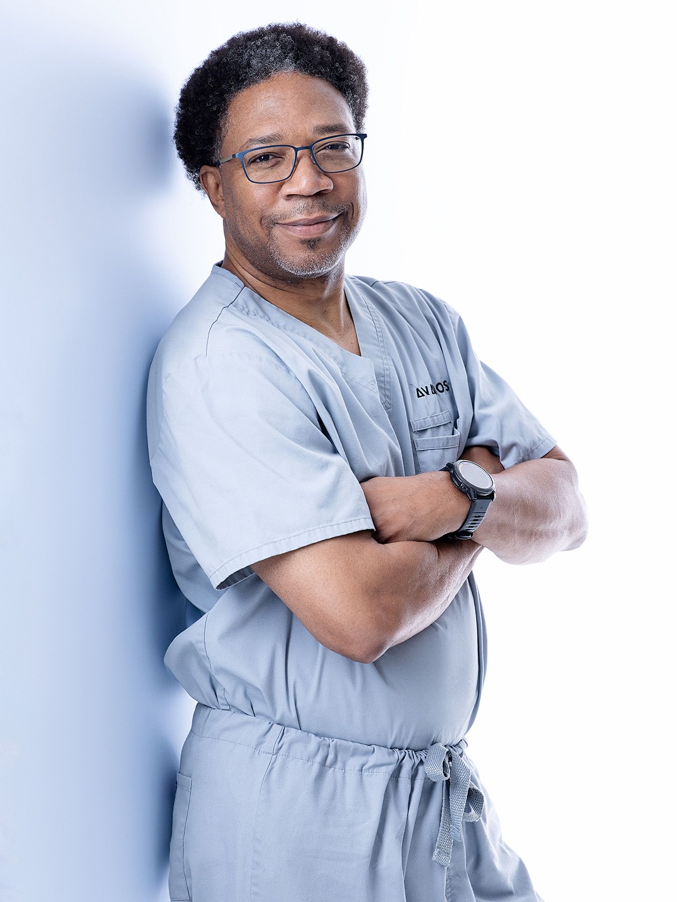 Healthcare professional in gray scrubs shown in multiple poses with arms crossed against white background.