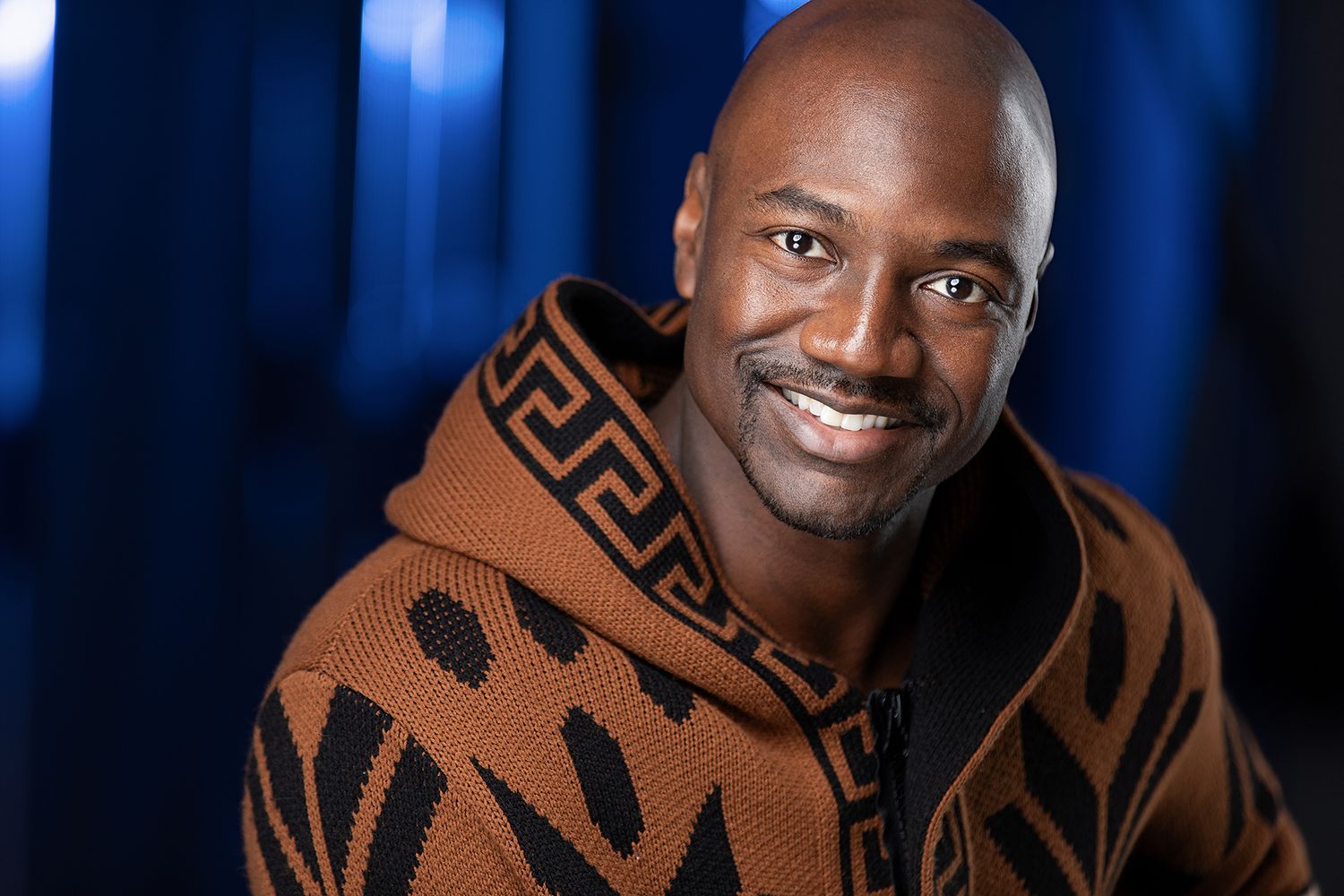Actor men headshot wearing a brown patterned sweater against a dark blue background. Cinematic headshot. Men photography in Atlanta.