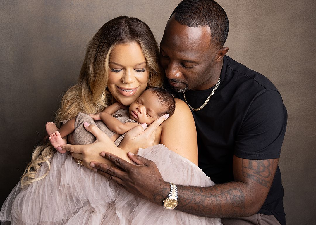 A couple tenderly holds their sleeping newborn baby wrapped in a soft pink blanket during a professional studio portrait session.