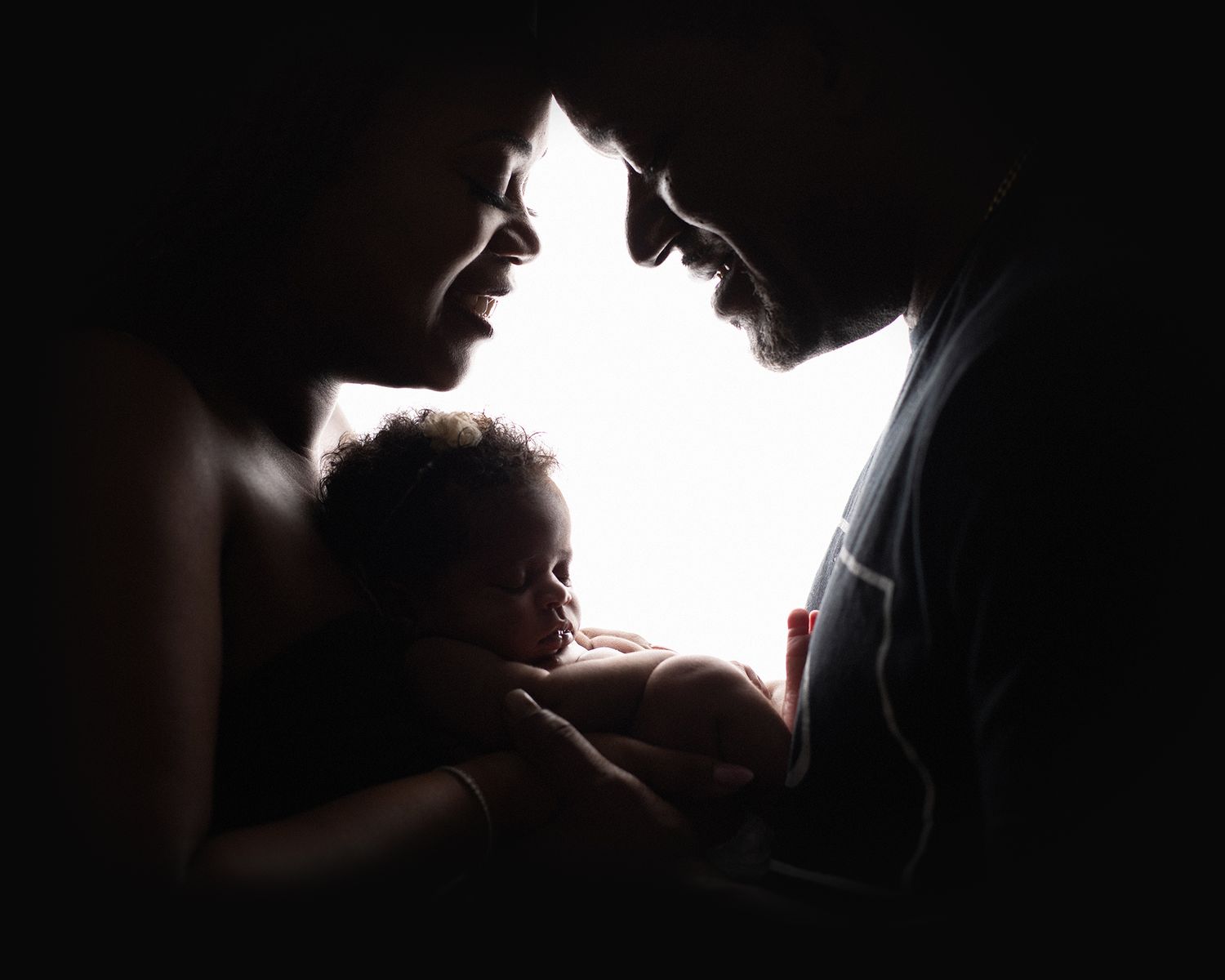 Silhouette of two parents cradling their newborn baby in a tender, backlit portrait.