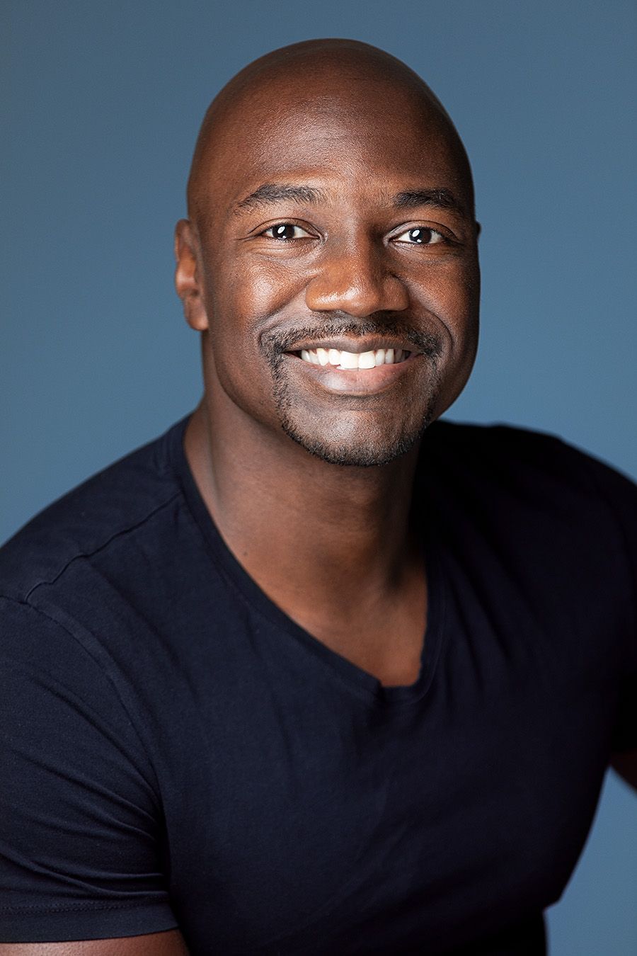 Atlanta men photography. Professional headshot of a person in a black v-neck shirt smiling warmly against a blue background.